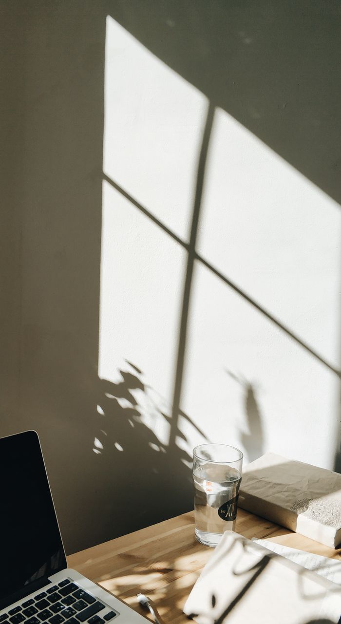 High angle shadows on wall near table with modern laptop arranged with book and water glass in cozy workspace